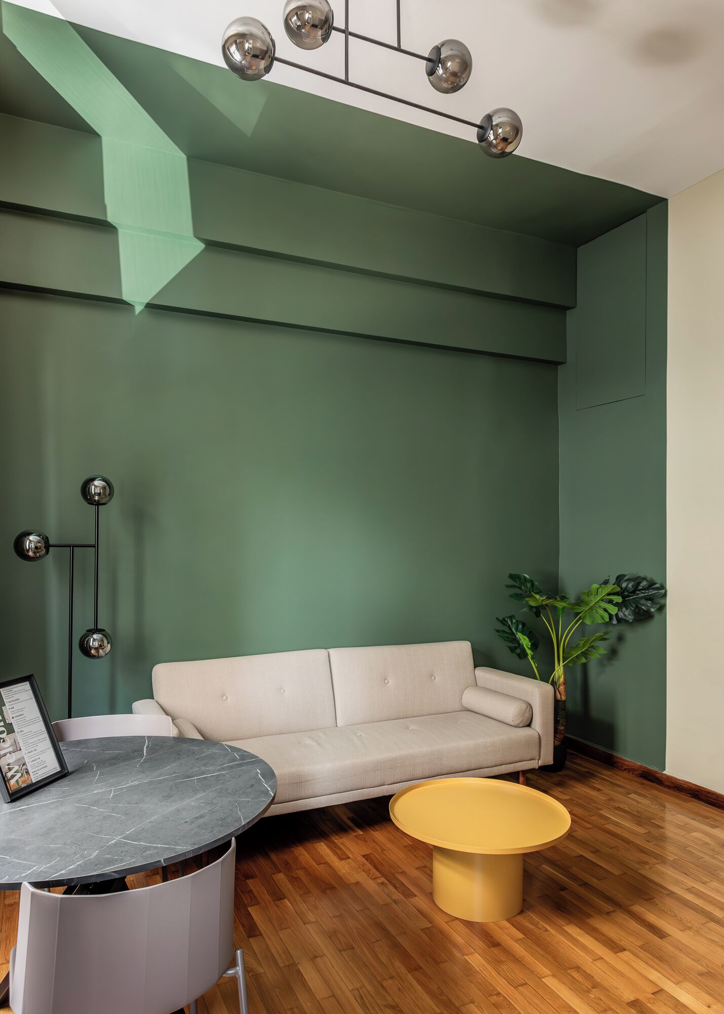 A modern living room with a green wall, a beige sofa, a marble table, and a yellow coffee table.