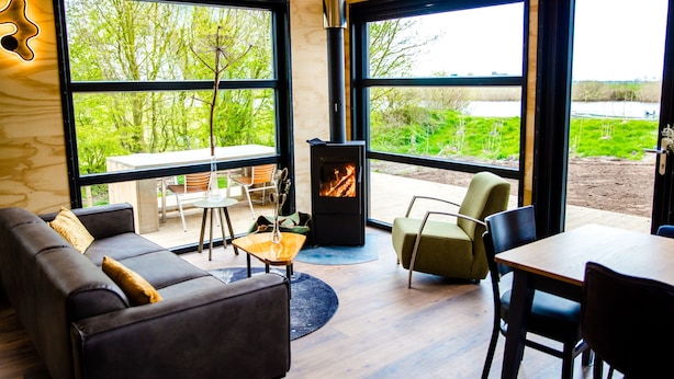 A modern living room with a fireplace, large windows, and a view of greenery. - Pean Huur je Eigen Schier Eiland (Nes)