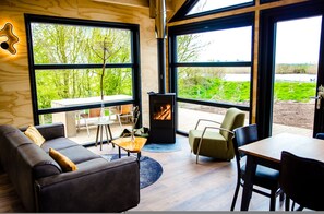 A modern living room with a fireplace, large windows, and a view of greenery. - Pean Huur je Eigen Schier Eiland (Nes)