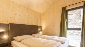Ein Schlafzimmer mit Holzboden, einem Bett mit weißer Bettwäsche, einem Nachttisch und einem Fenster mit Vorhang.