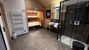 A modern bathroom with a glass shower enclosure, a wooden sauna area, and a sink with a towel.