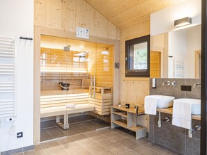 Une salle de bain moderne avec un lambris en bois, un sauna et un meuble-lavabo à deux vasques.