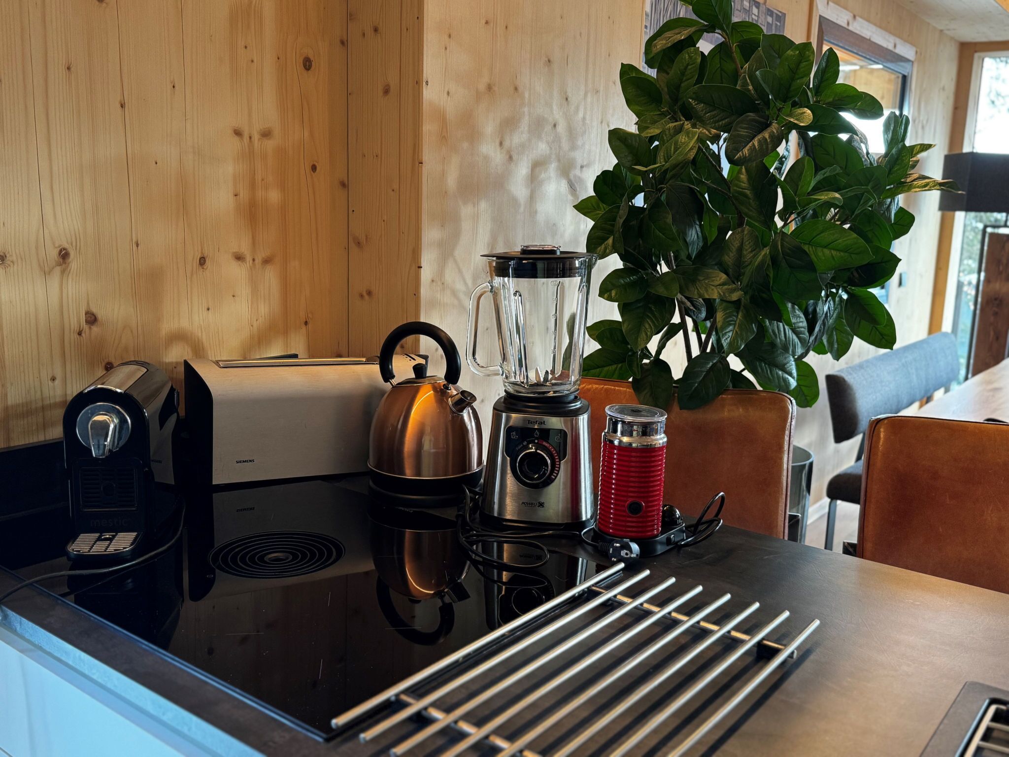 A kitchen with a Siemens toaster, a kettle, a blender, a red thermos, and a plant.