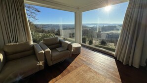 A modern room with a large window, a beige sofa, and a wooden floor. - Panoramic villa with private sauna in Erezée (Érezée)