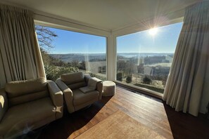 A modern room with a large window, a beige sofa, and a wooden floor. - Panoramic villa with private sauna in Erezée (Érezée)