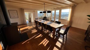 A spacious dining area with a long table, multiple chairs, and a view of the outdoors through large windows. - Panoramic villa with private sauna in Erezée (Érezée)