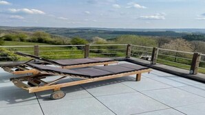 A wooden deck with two sun loungers, a metal railing, and a view of rolling hills. - Panoramic villa with private sauna in Erezée (Érezée)