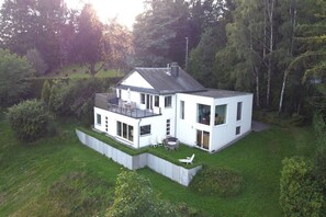A modern two-story house with a flat roof, large windows, and a small deck.