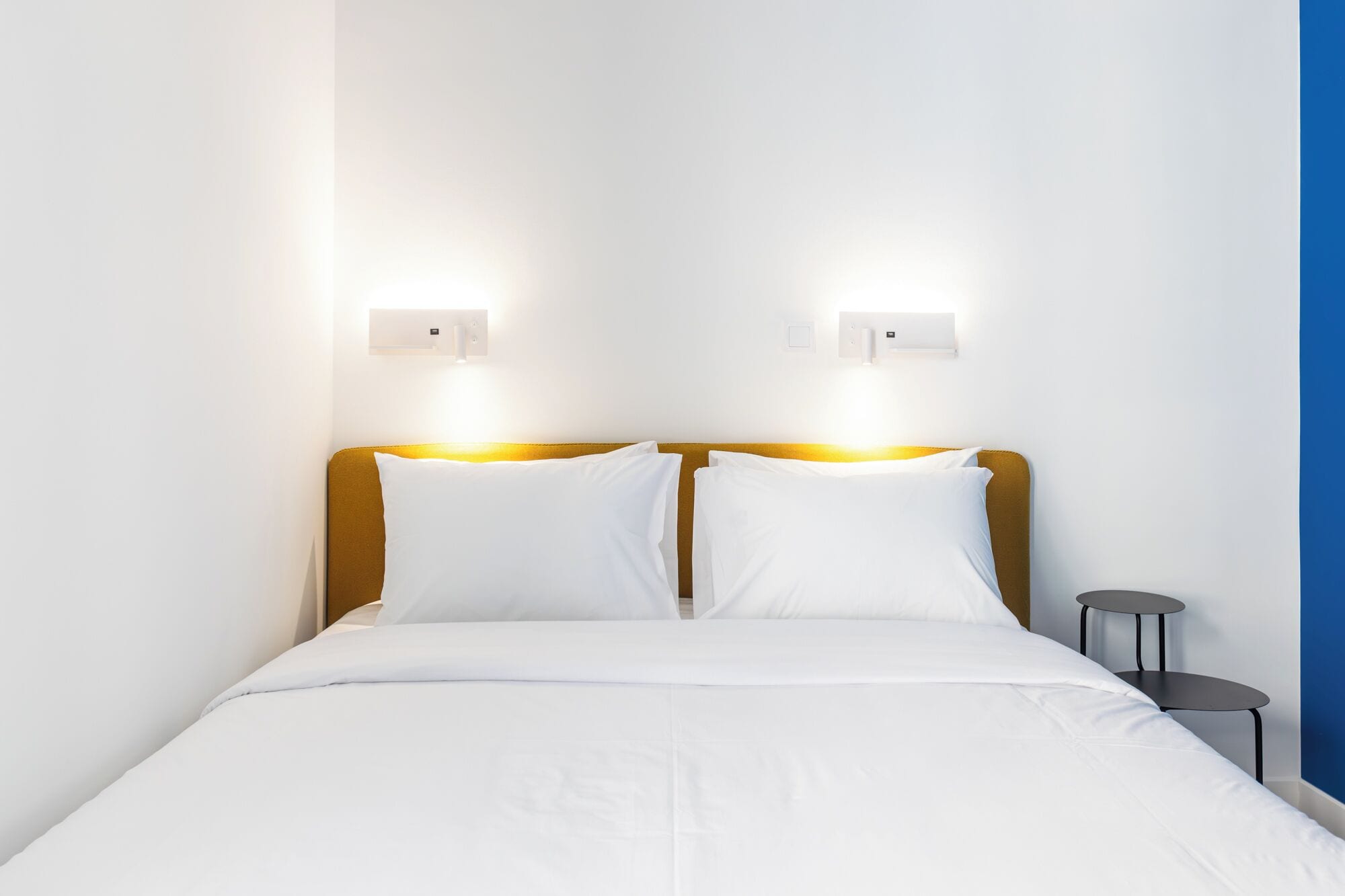 A hotel room with a bed, two bedside lamps, a small table, and a wall-mounted light fixture.