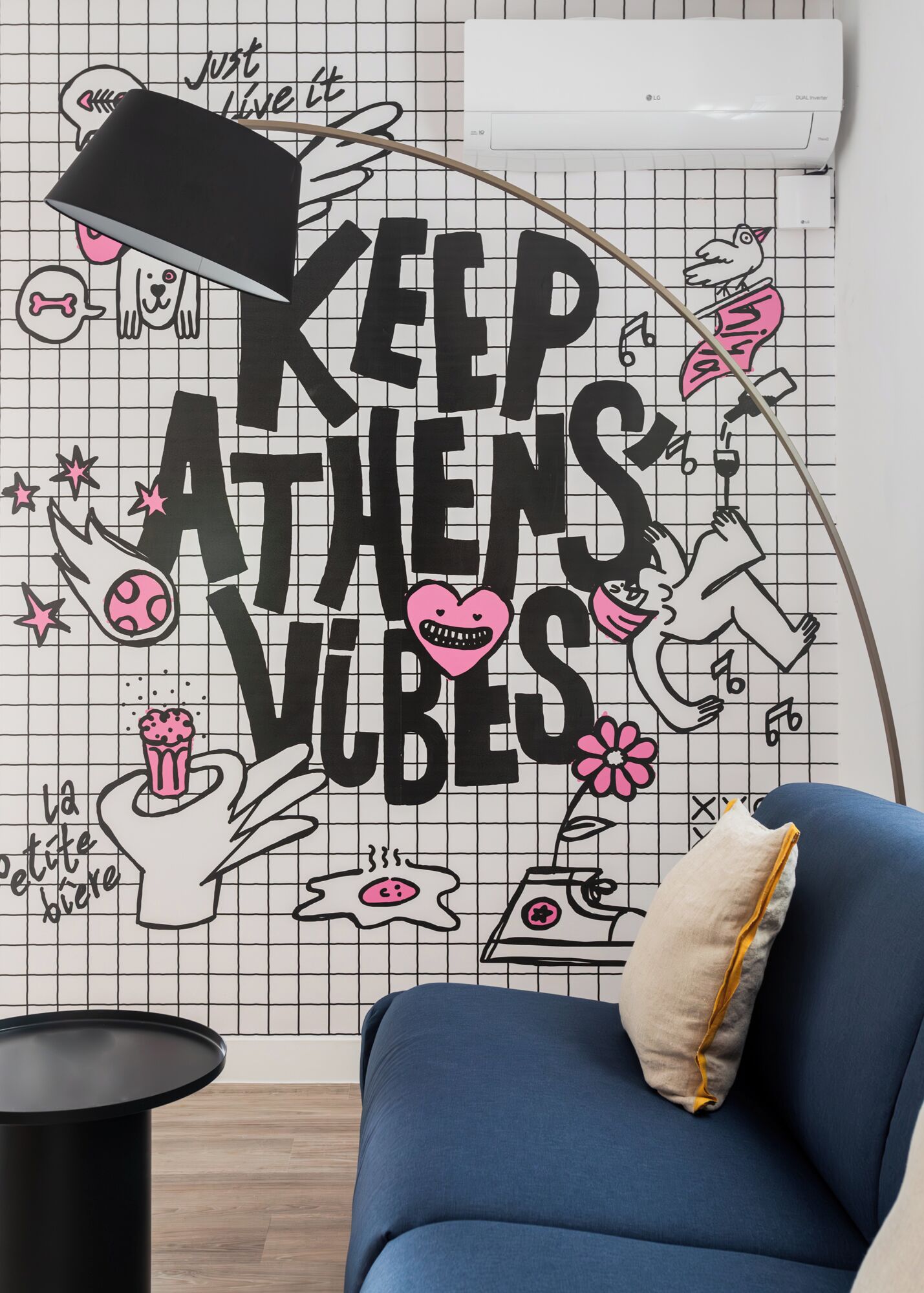 A room with a blue sofa, a black lamp, and a wall with a grid pattern and various doodles.