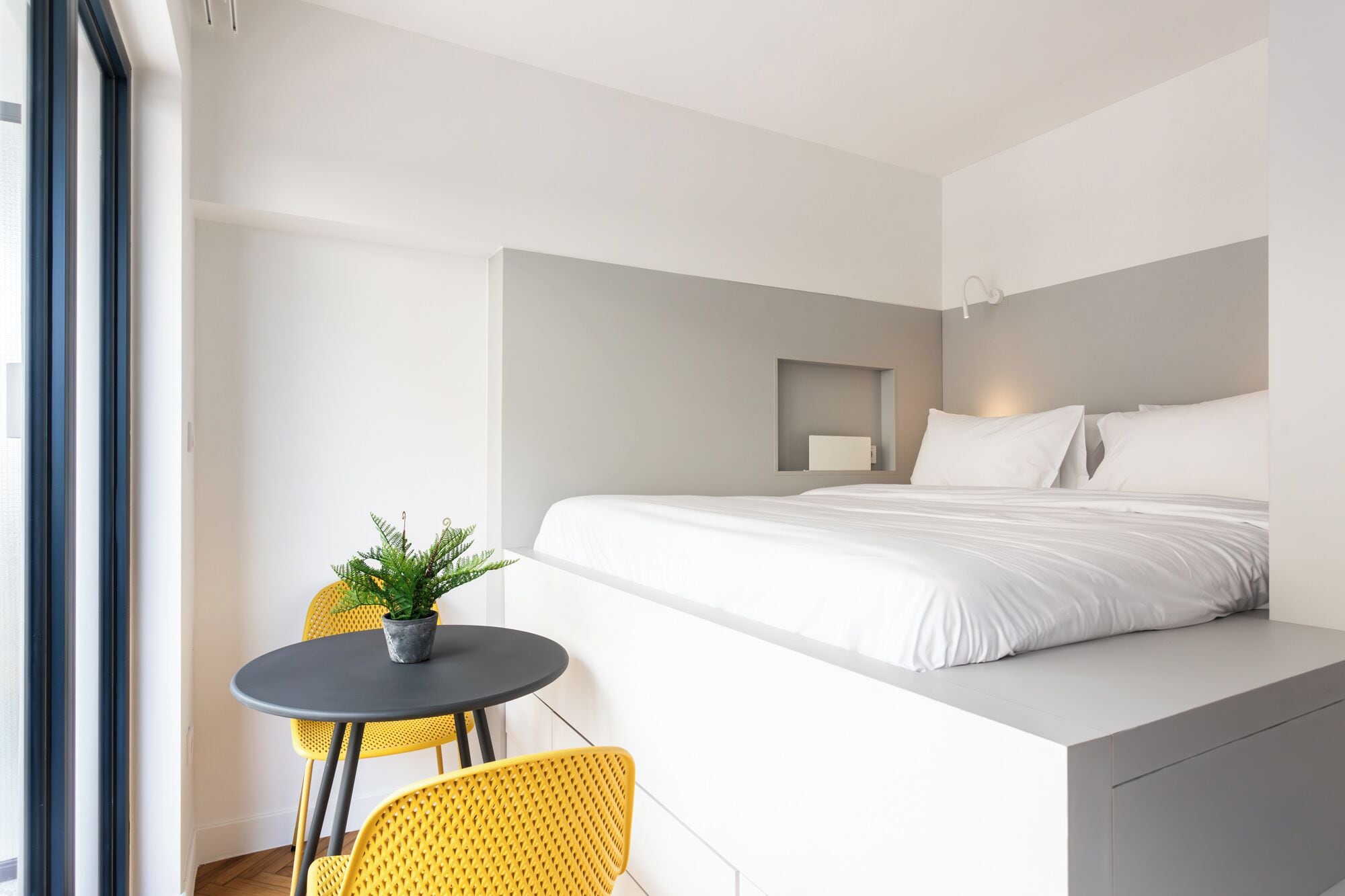 Una habitación de hotel moderna con una cama grande, una mesita con sillas y una planta en maceta.