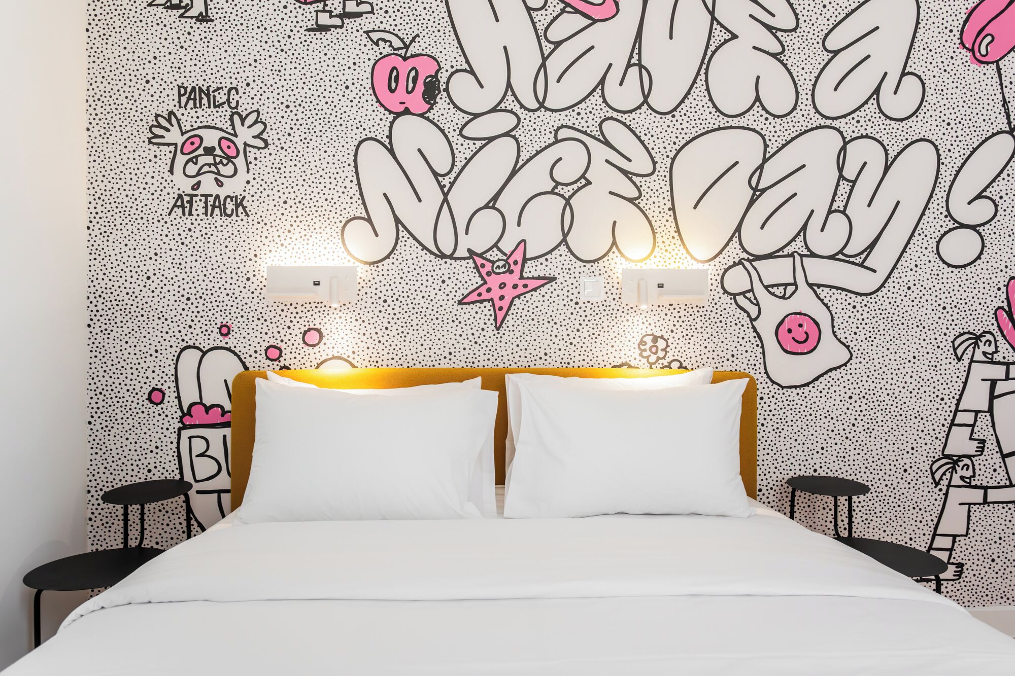 A bedroom with a bed, two bedside tables, a wall with a polka dot pattern, and cartoonish wall art.