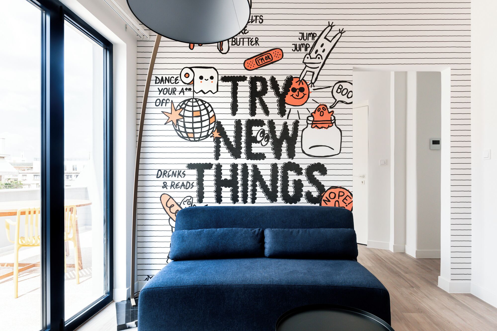 A modern room with a large window, a blue sofa, and a wall with a motivational quote and doodles.