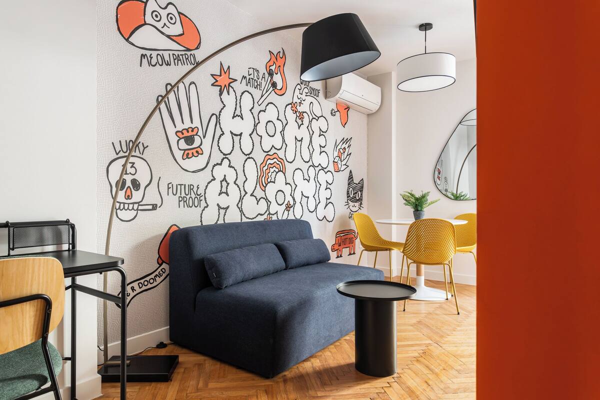Una sala de estar moderna con un sofá azul, una mesa de centro redonda negra y un mural con dibujos caricaturescos.