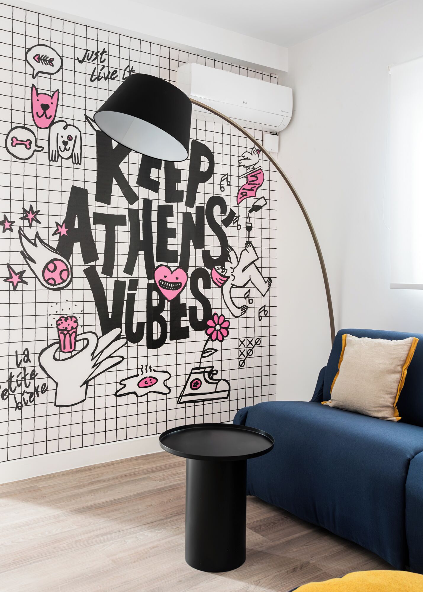 Une pièce avec un mur orné d’un motif en quadrillage, une lampe noire, un canapé bleu et une petite table noire.