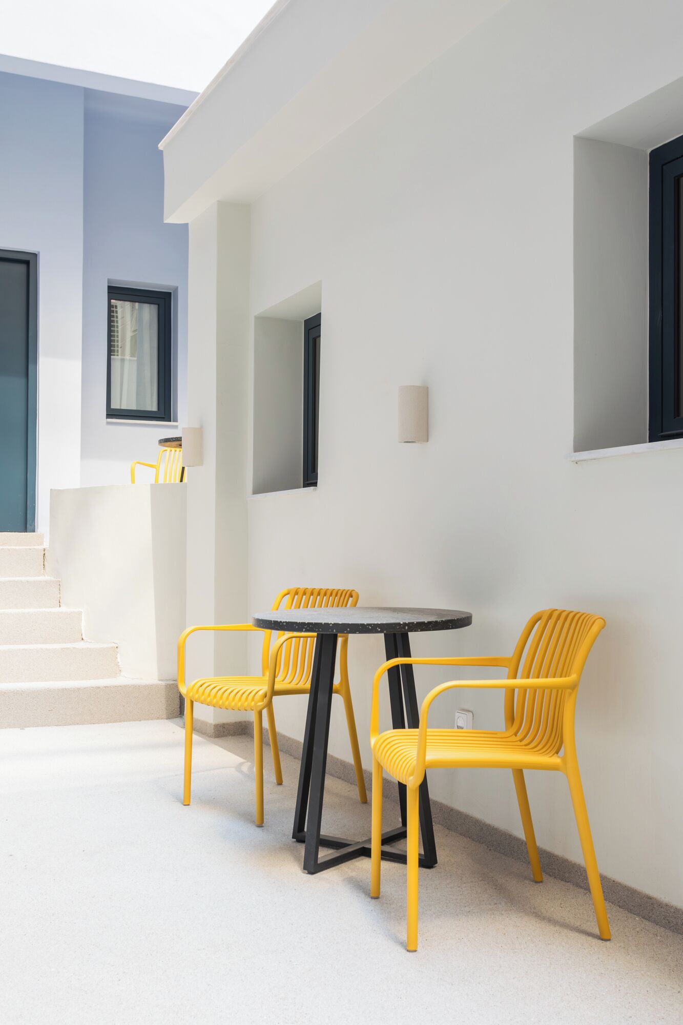 A modern outdoor seating area with a round table and four yellow chairs.