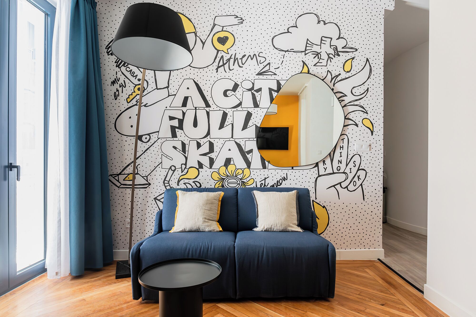 Una sala de estar moderna con un sofá azul, una mesa de centro negra redonda y una pared con un patrón juguetón de lunares y un gran texto que dice "A CITY FOR YOU".