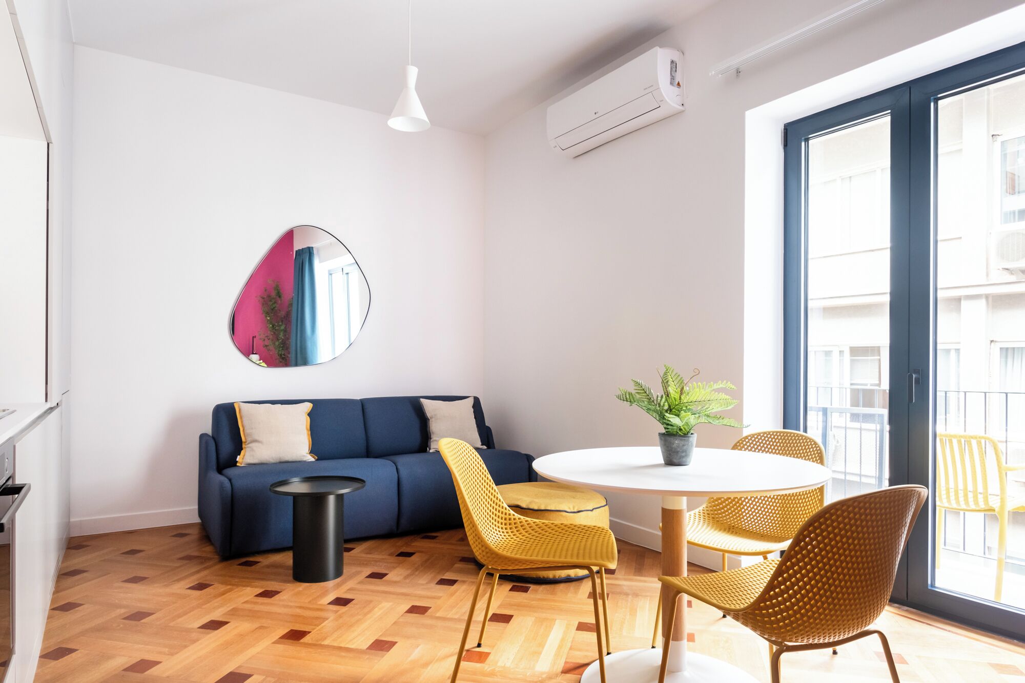 A modern living room with a blue sofa, a round white table, and yellow wicker chairs.