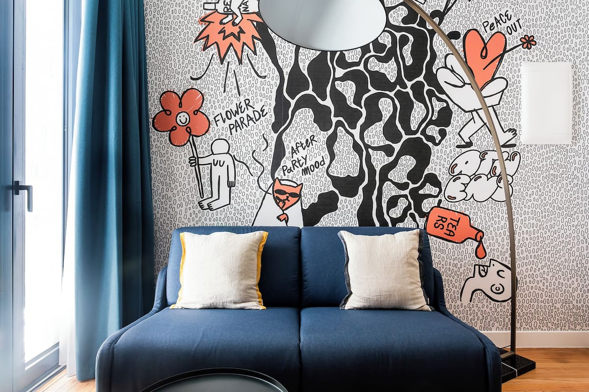 Un dormitorio moderno con un sofá azul, papel tapiz estampado y una lámpara de pie.