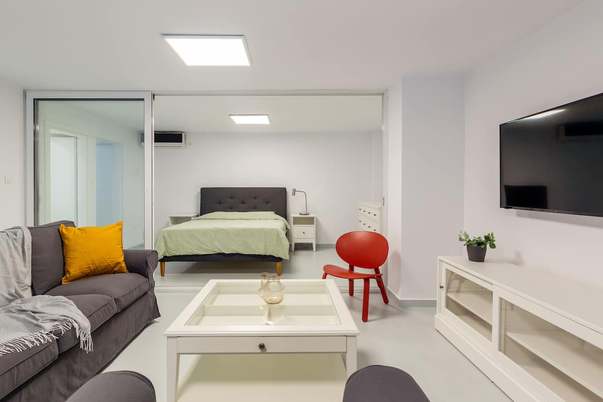 A modern, well-lit bedroom with a bed, bedside table, and a TV mounted on the wall.