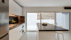 A modern kitchen with white cabinets, a black countertop, and a large window. - Kookaki by Zoia Living (Athens)
