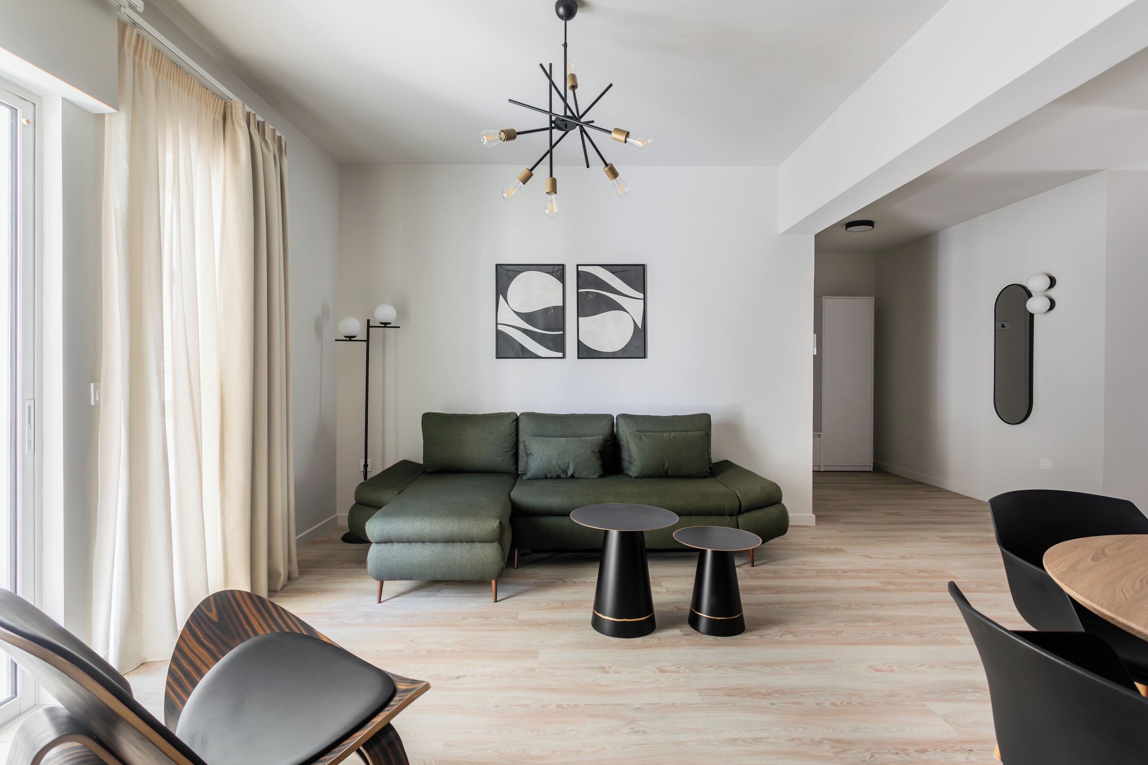 A modern living room with a sectional sofa, two black side tables, and a wooden dining table.