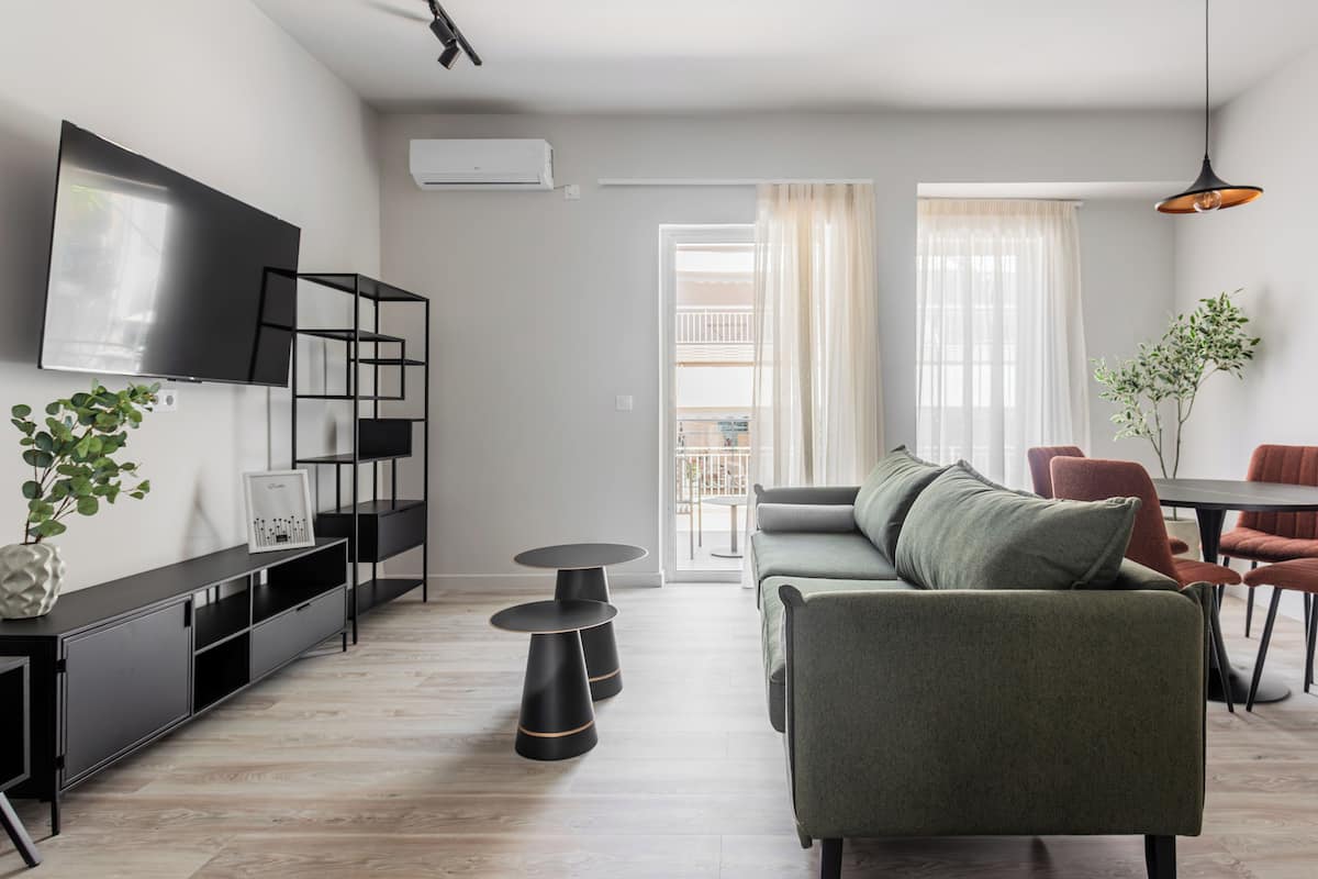 A modern living room with a sofa, a TV mounted on the wall, a plant, and a dining area with chairs and a table.