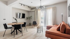 A modern living room with a sofa, a dining table with chairs, a TV mounted on the wall, and a plant. - Kookaki by Zoia Living (Athens)