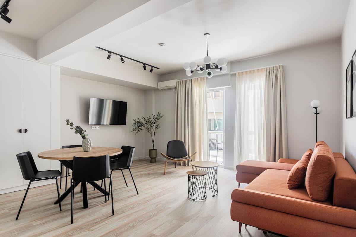 A modern living room with a sofa, a dining table with chairs, a TV mounted on the wall, and a plant.