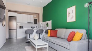 A modern living room with a grey sofa, a white coffee table, and a green accent wall. - Snug by Zoia Living (Athens)