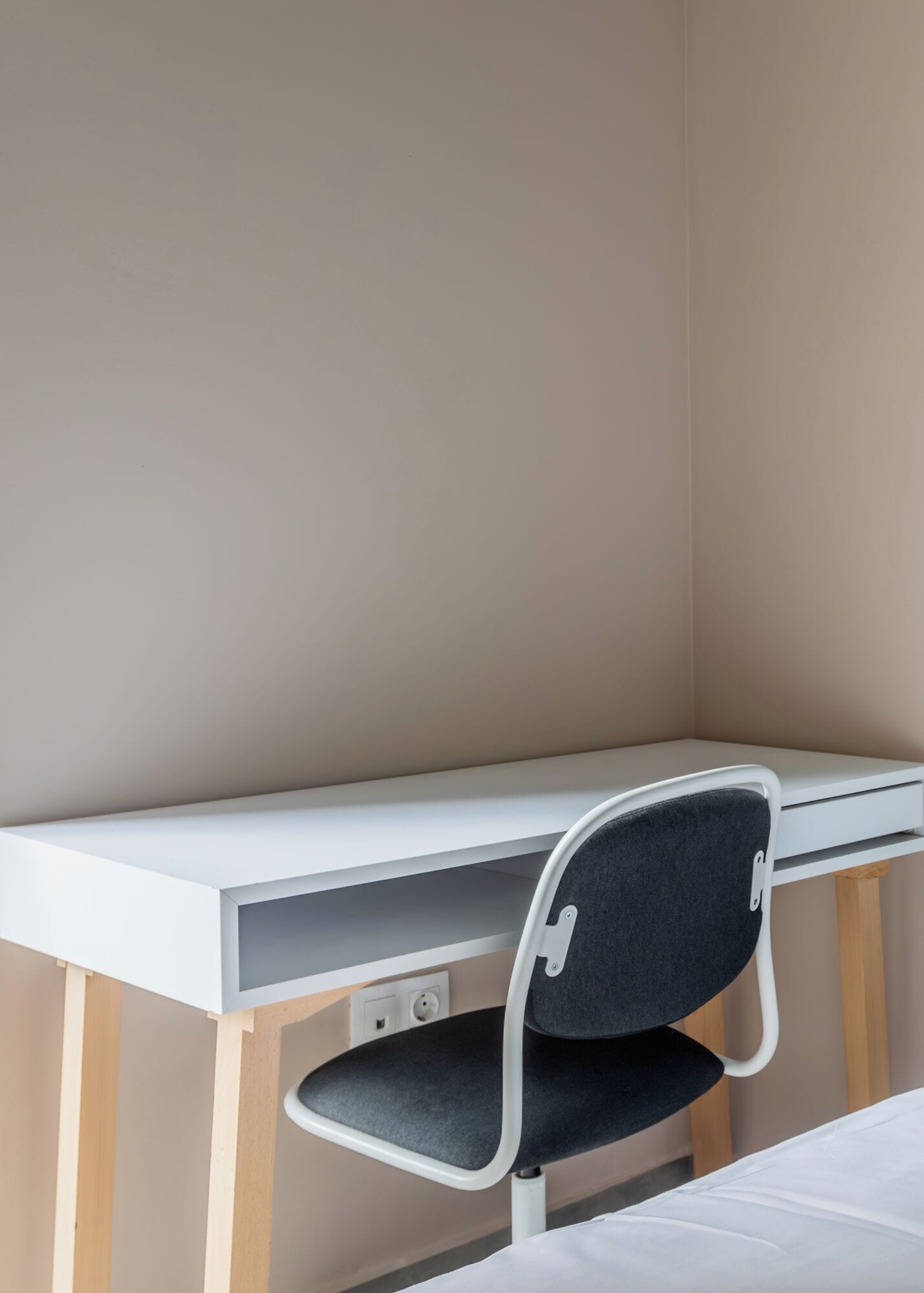 A corner desk with a chair, a bed, and a wall.