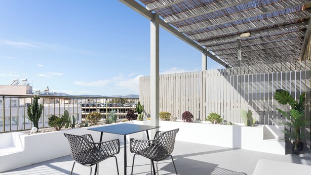 A rooftop patio with a table and chairs, surrounded by potted plants and a white fence. - Snug by Zoia Living (Athens)