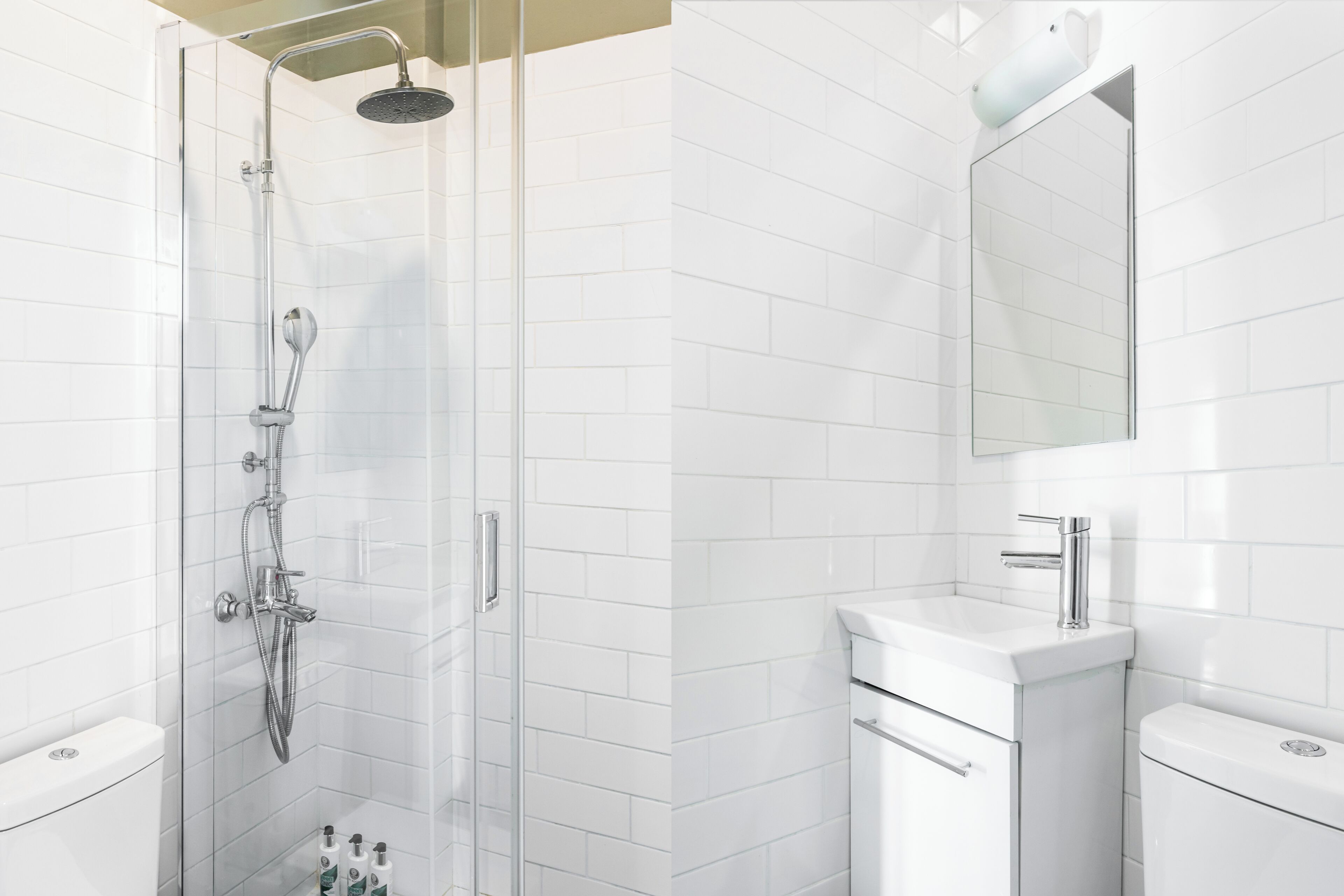 Un baño moderno con ducha de vidrio, paredes de azulejos blancos, un lavabo blanco y un espejo sobre el lavabo.