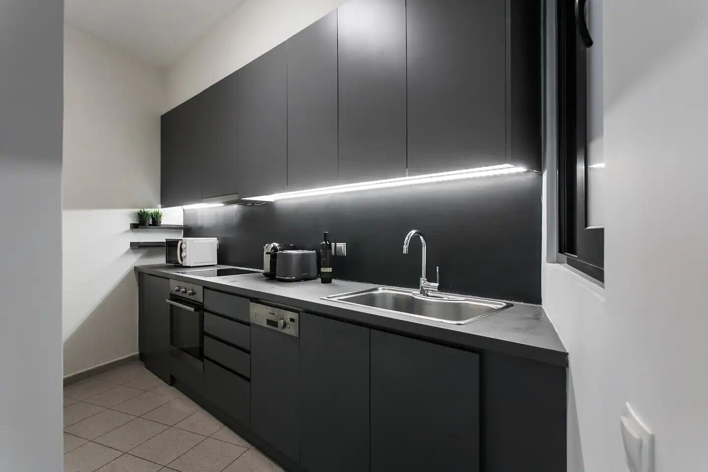 Una cucina moderna con mobili scuri, un lavello in acciaio inossidabile e un forno integrato.