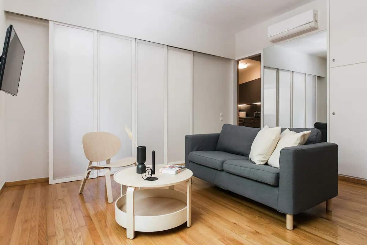 A modern living room with a grey sofa, a small round table, and a wooden floor.