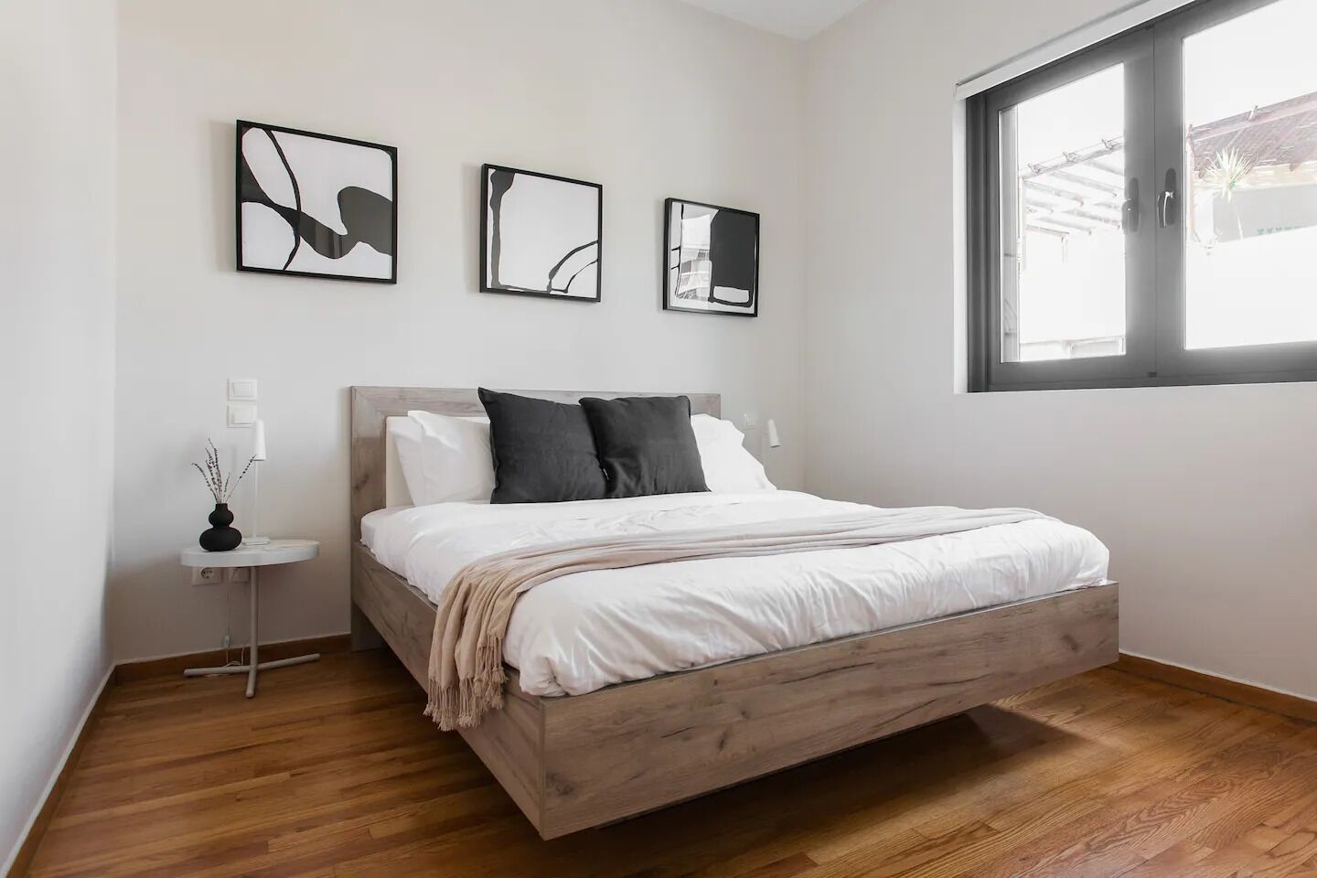 A bedroom with a wooden bed, white bedding, and three abstract wall art pieces.