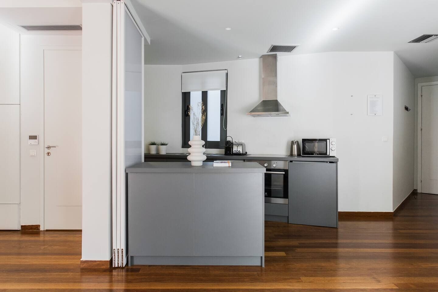 Una cocina moderna con armarios grises, horno empotrado, microondas y campana extractora de acero inoxidable.