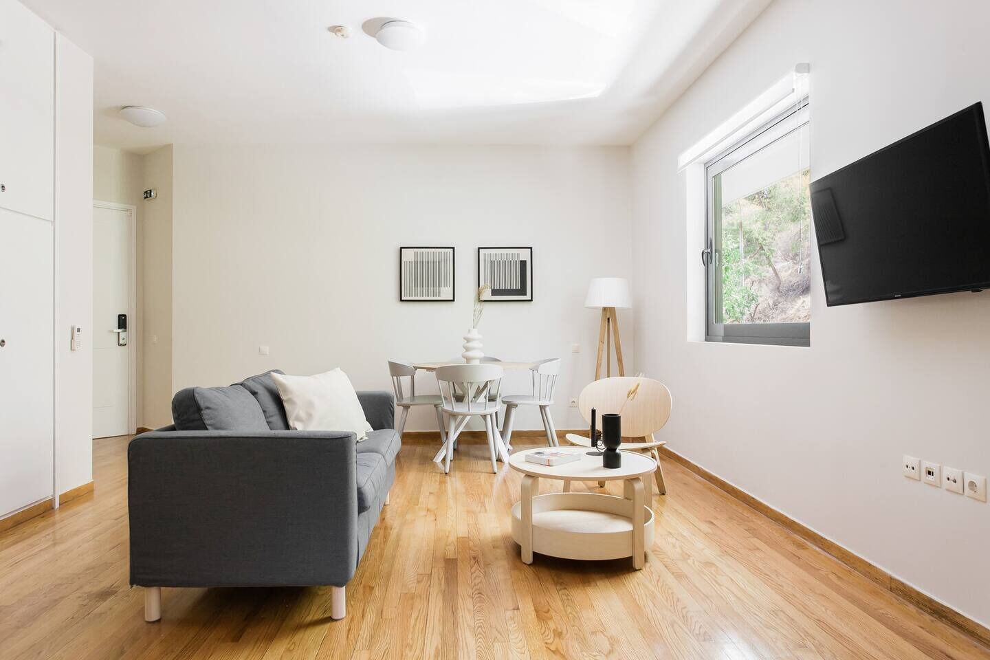 A modern living room with a grey sofa, a round coffee table, and a TV mounted on the wall.