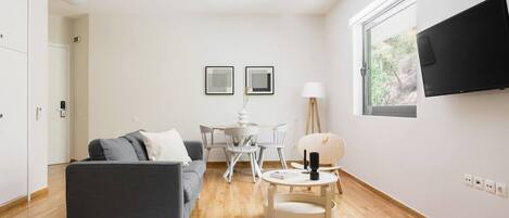 A modern living room with a grey sofa, a round coffee table, and a TV mounted on the wall.