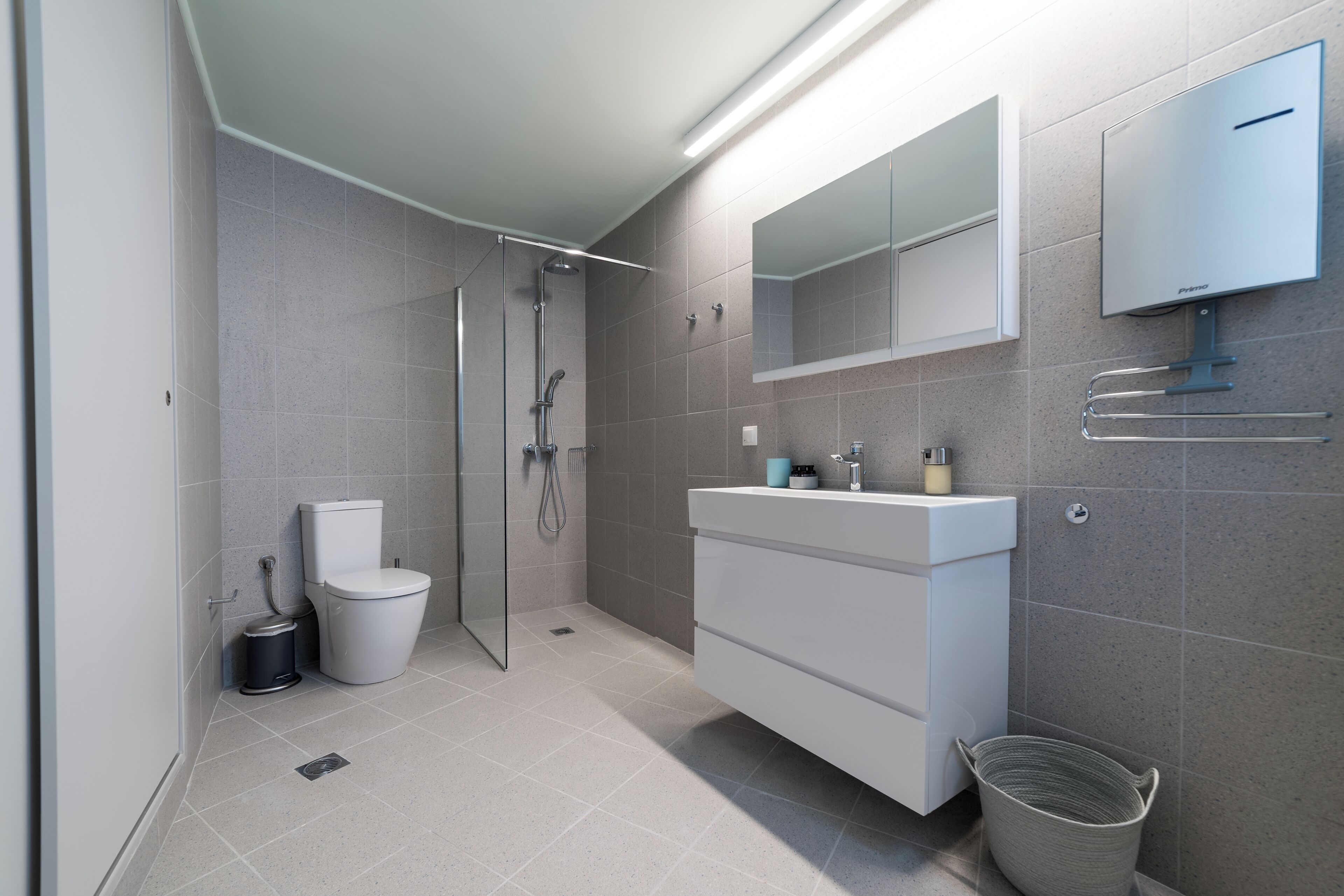Ein modernes Badezimmer mit einer gläsernen Duschkabine, einem weißen Waschbecken und einem Spiegel über dem Waschtisch.