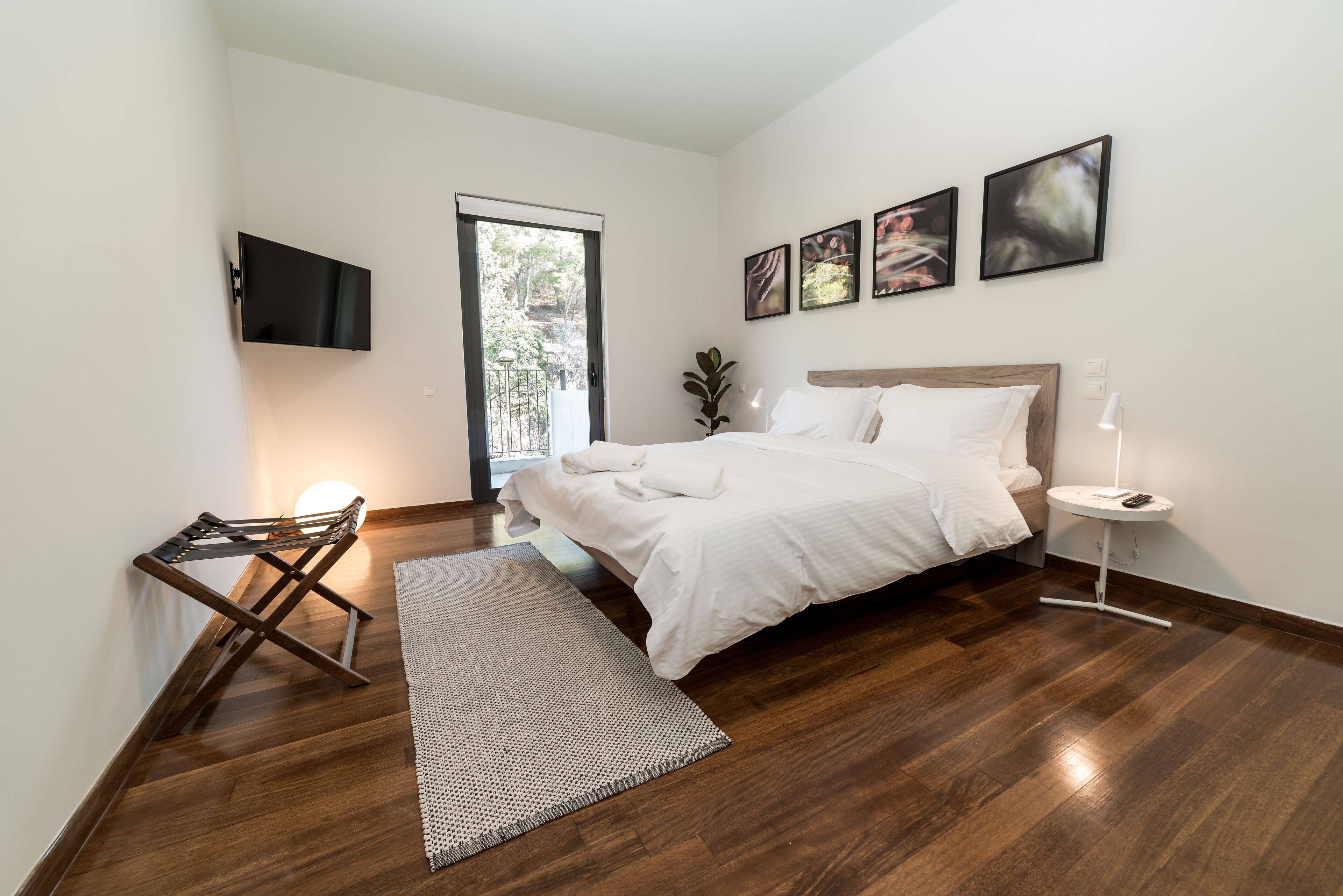 Une chambre avec un lit, un téléviseur fixé au mur, une petite table avec une lampe et une fenêtre donnant sur un paysage verdoyant.