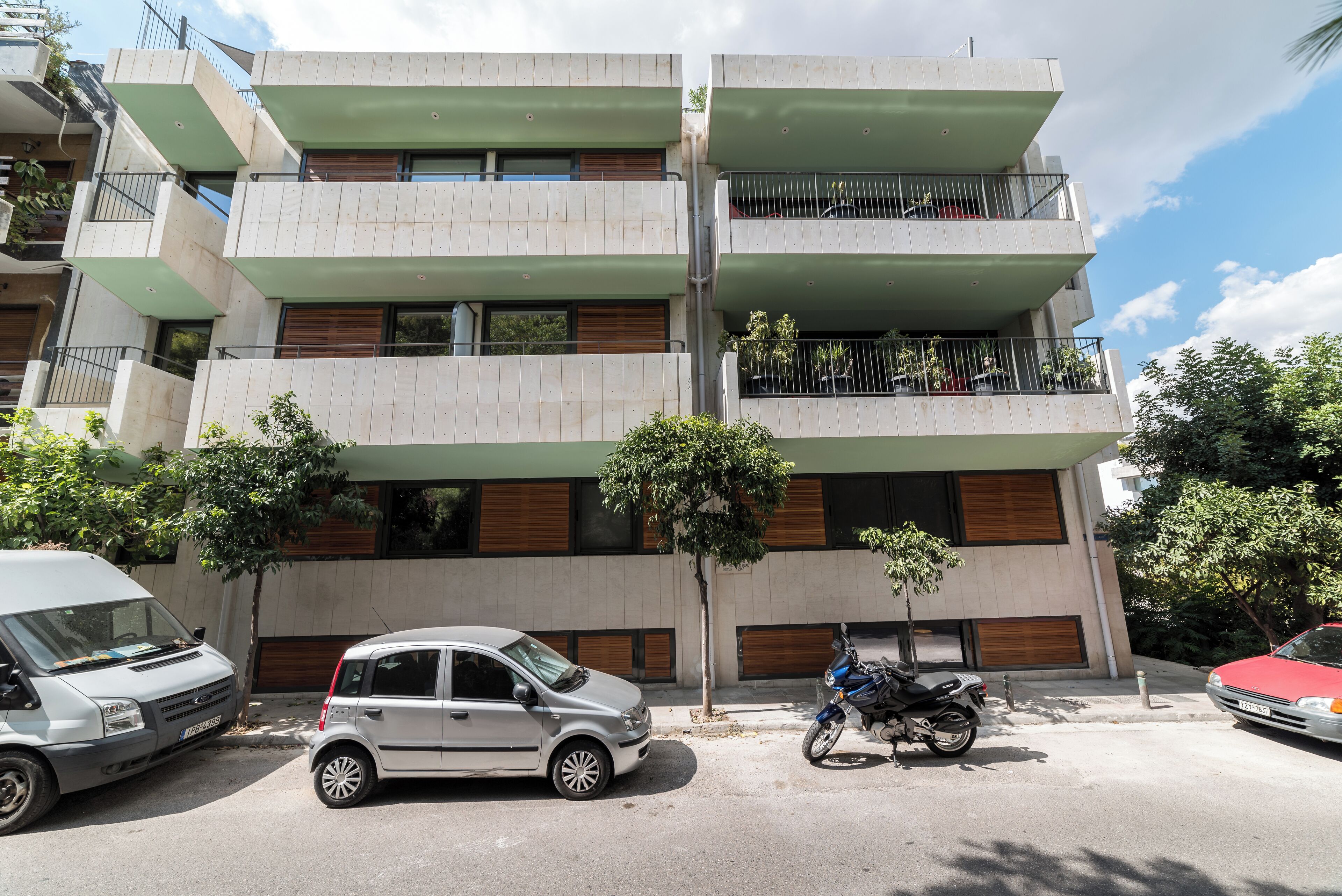 A multi-story building with balconies, parked cars, and a motorcycle.