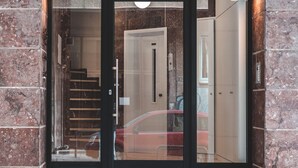 A modern building entrance with a glass door, a staircase, and a red car parked outside. - OneZeroTwo by Zoia Living (Athens)