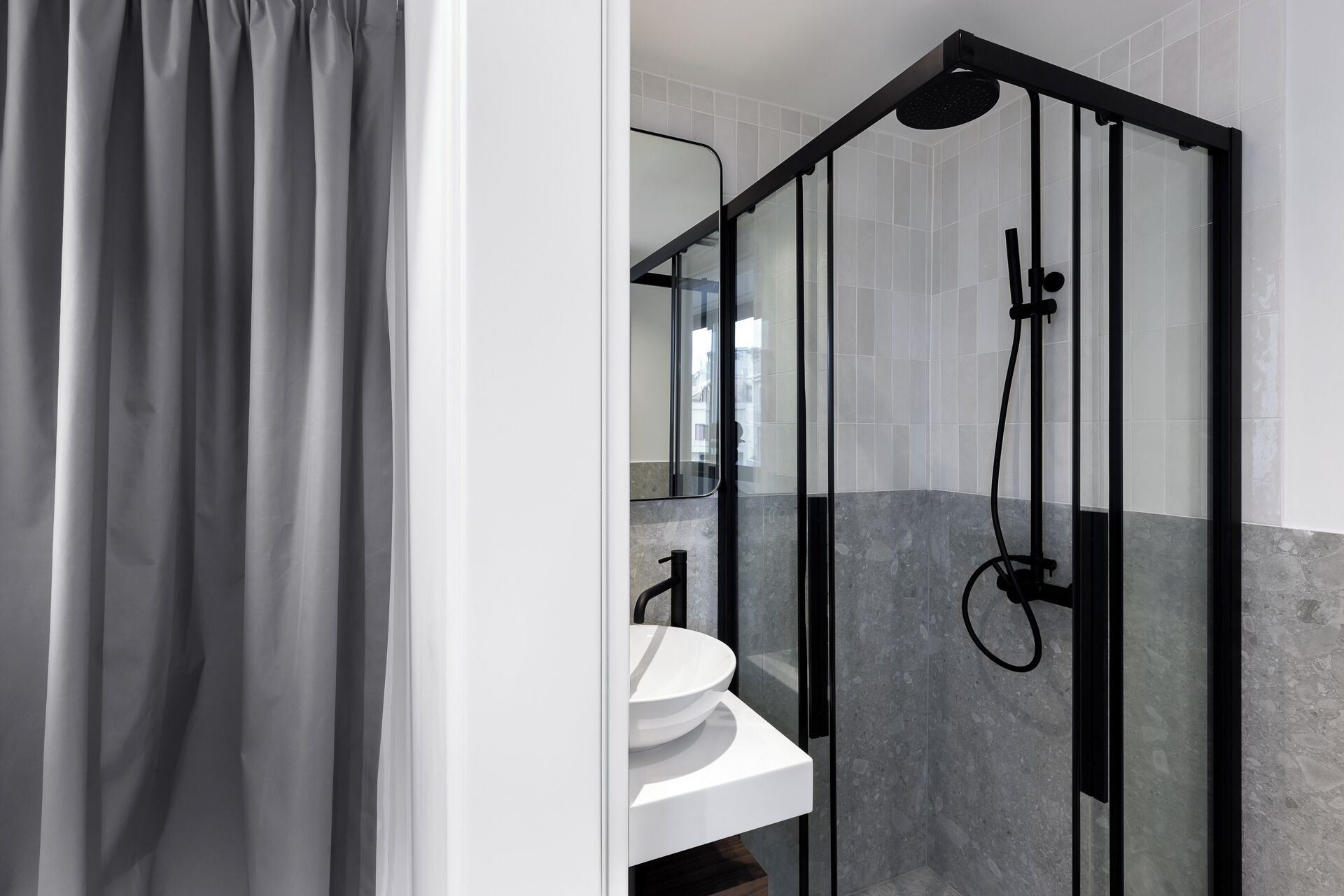 Un baño moderno con ducha de vidrio, un lavamanos blanco y un espejo.