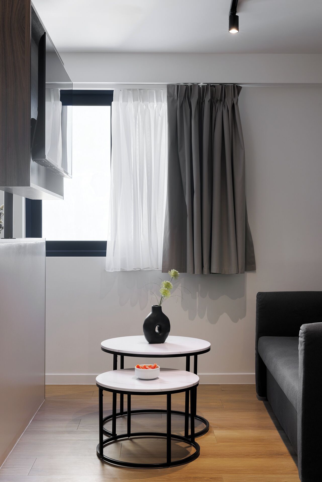 Una sala de estar moderna con una mesa redonda, un sofá negro y una ventana con cortinas.