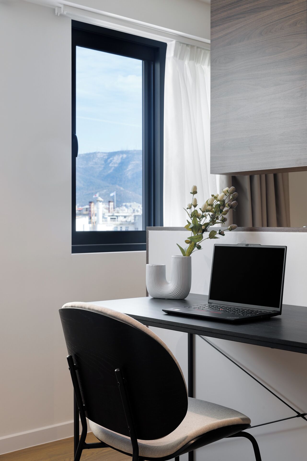 Een moderne kantoorruimte met een bureau, laptop en een stoel. Een raam toont een uitzicht op een stad en bergen.