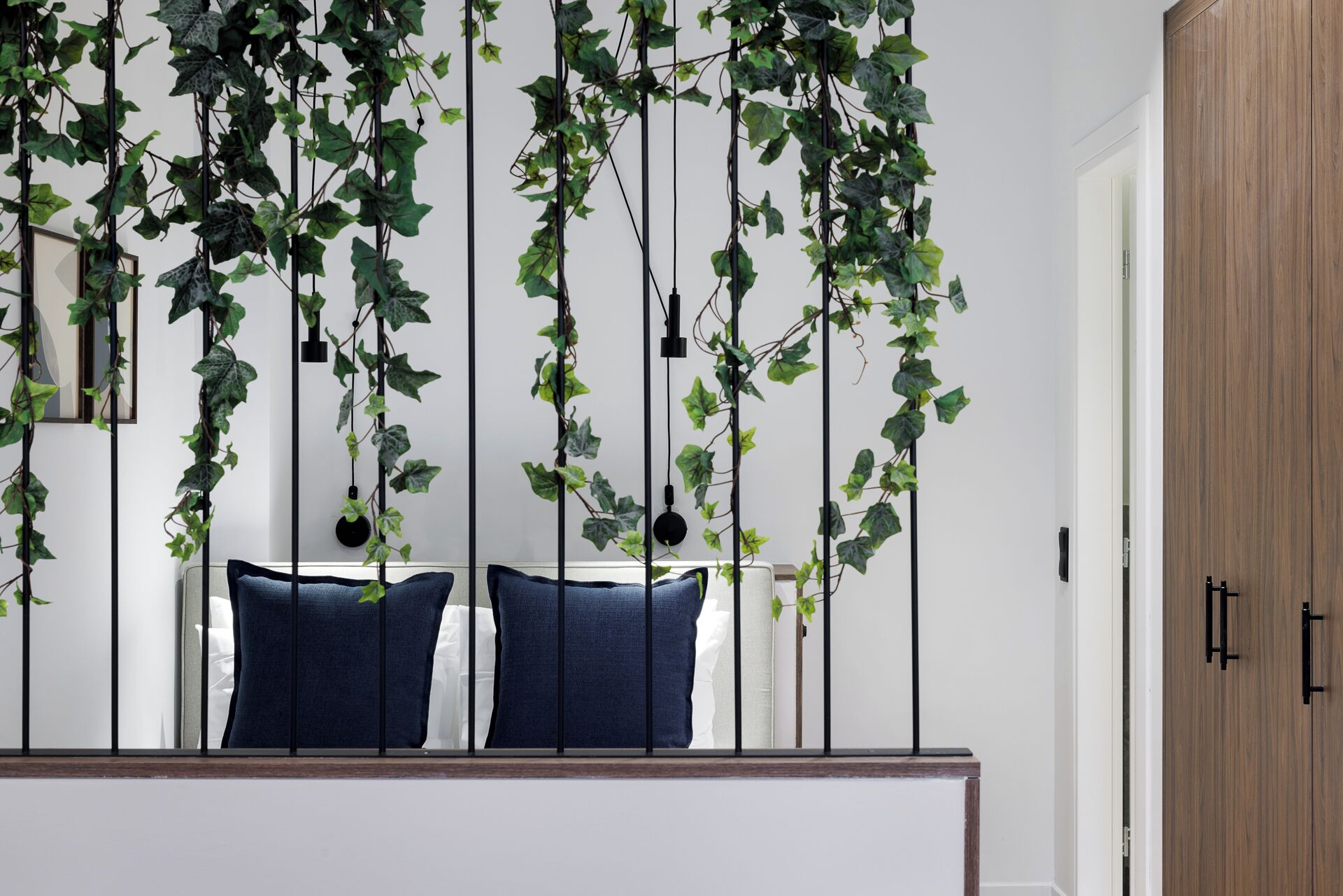 A bedroom with a bed, two pillows, a wooden door, and a wall adorned with hanging vines.