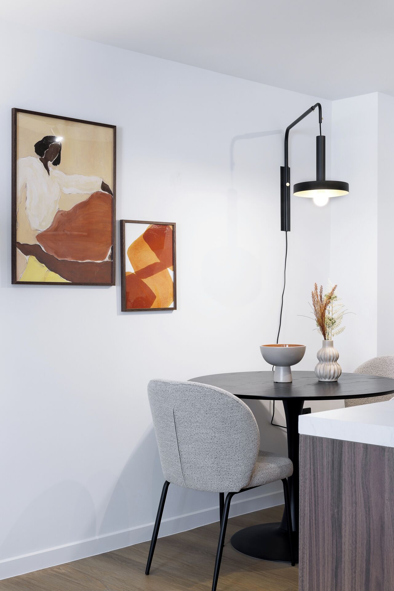A modern dining area with a round table, a gray upholstered chair, and two abstract paintings on the wall.