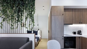 Ein modernes Hotelzimmer mit einer Sitzecke, einem Sessel, einem Bett und einer Küchenzeile inklusive Kaffeemaschine und Backofen.