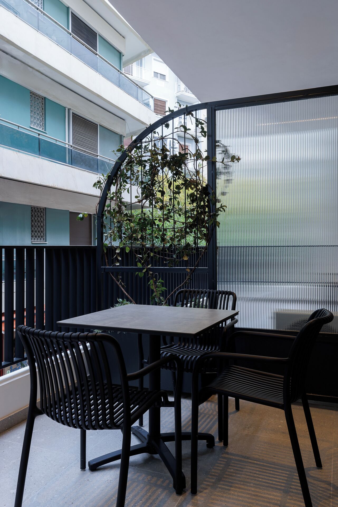 A balcony with a table and chairs, a view of a building, and a plant.